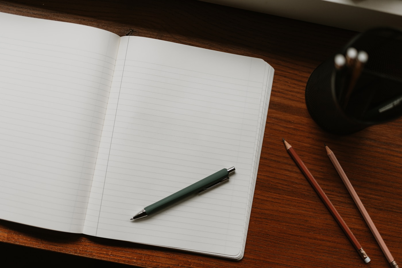 Ein aufgeschlagenes Notizbuch mit Stift und Bleistiften auf einem Holztisch